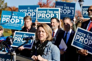 EANY Deputy Director Kate Kurera Speaks at Press Conference Surrounded by Signs Saying "Vote Yes for Prop 1"